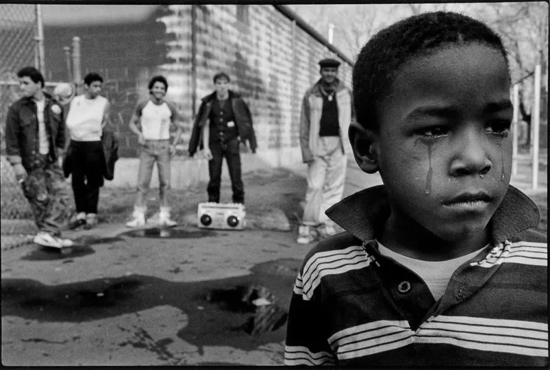 Monochrome shot of street kid in tears as gang or tormentors look on.