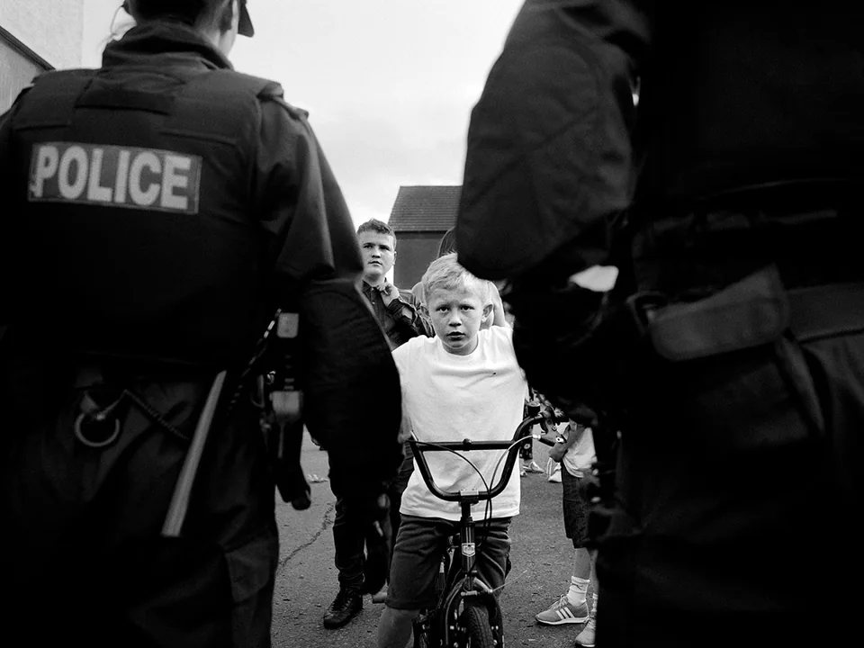 Street photography in black and white, capturing a a young boy on a bike confronting police.
