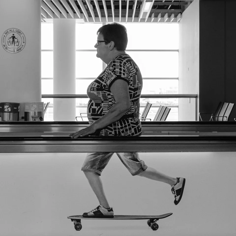 Candid black and white photo of a woman on a moving walkway - or is it a skateboard?