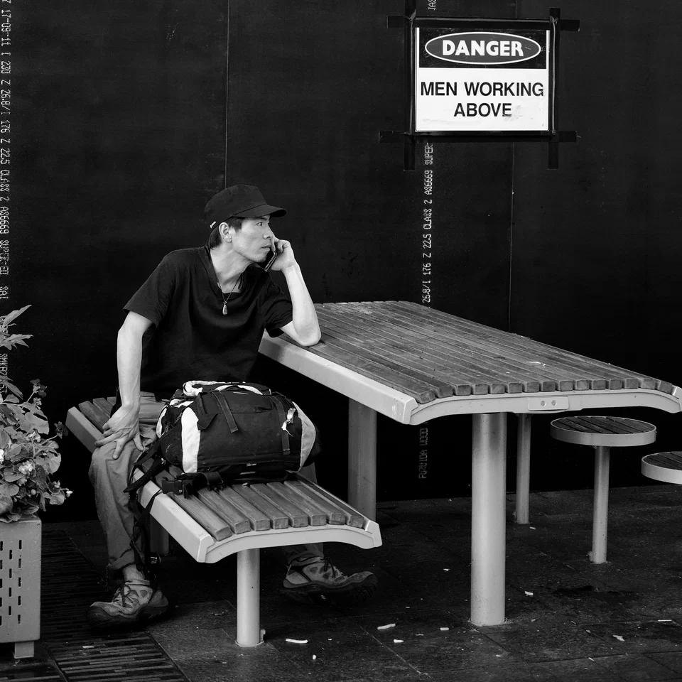 A person sits beneath a construction warning sign — photograph by Peter Pickering