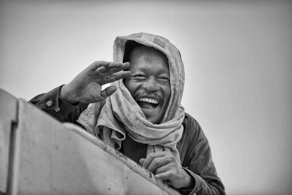 A smiling man raises his hand beside his face — photograph by Peter Pickering