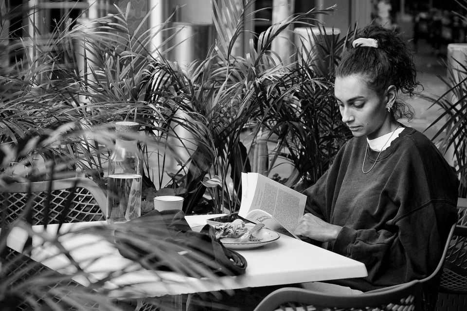 A woman reads a book at a café table — photograph by Peter Pickering