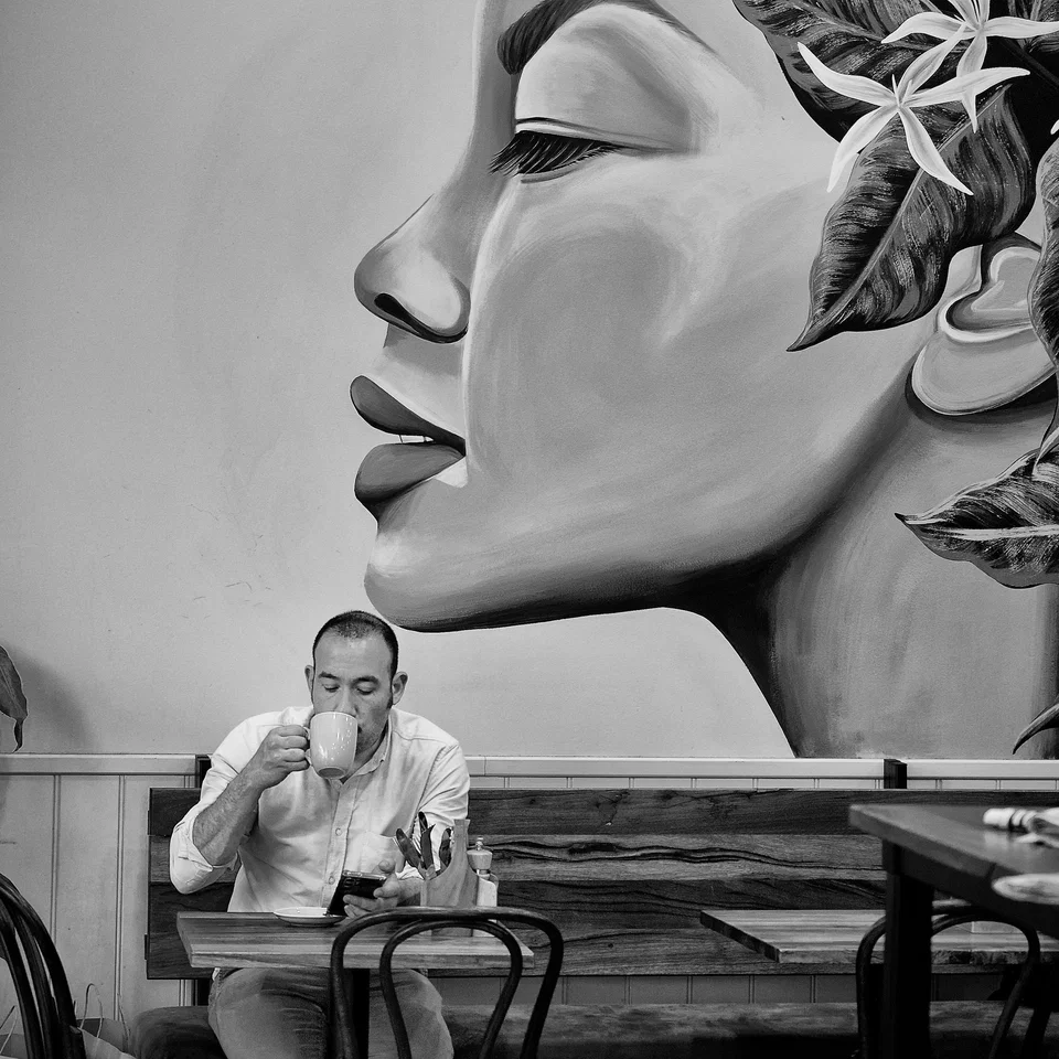 A seated man beneath a mural of a large face — photograph by Peter Pickering