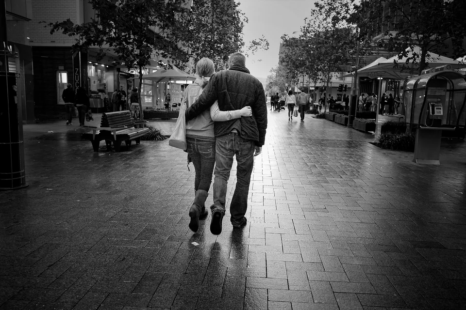 Two people walk together on a rain-darkened shopping street — photograph by Peter Pickering