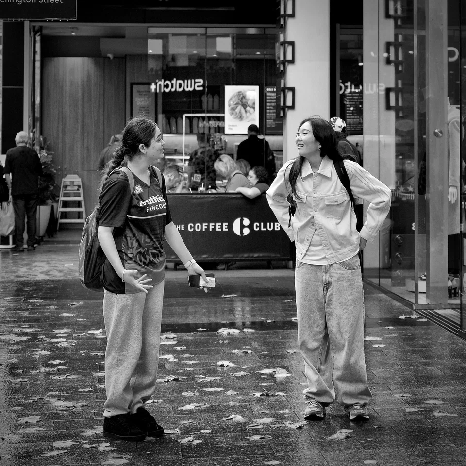Two people talk on rain-wet paving outside a café — photograph by Peter Pickering