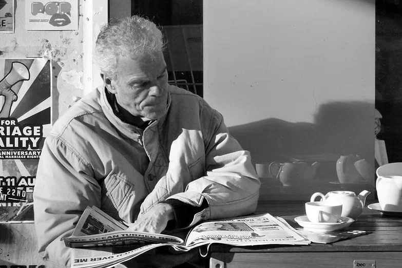 A man reads a newspaper at an outdoor café table — photograph by Peter Pickering
