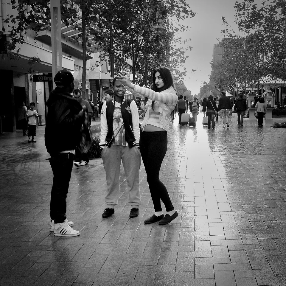 People pause in a sunlit shopping street — photograph by Peter Pickering