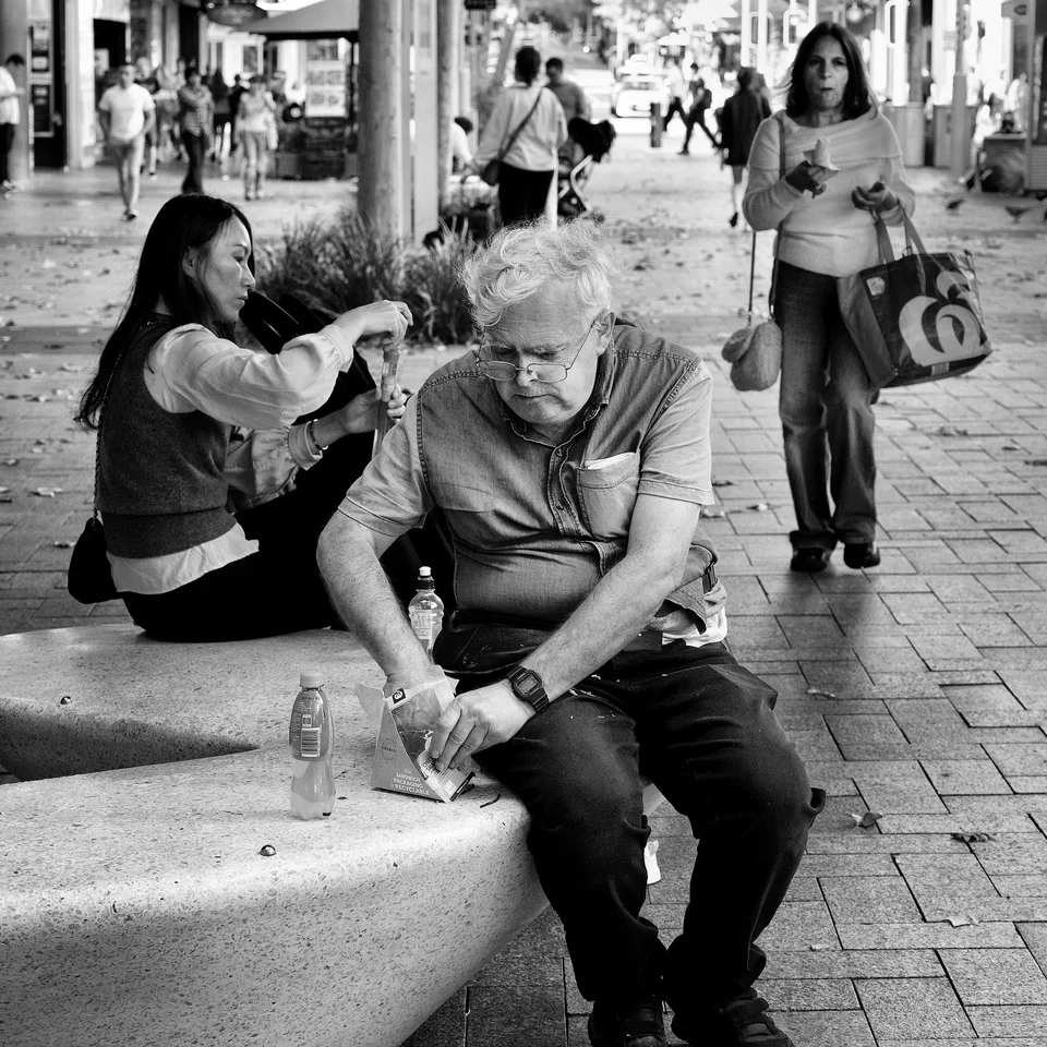 A seated man surrounded by activity on the pavement — photograph by Peter Pickering