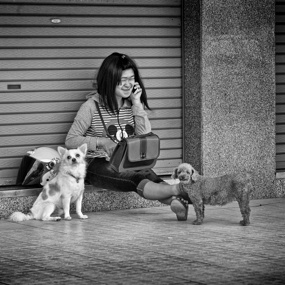 A woman sits with two dogs beside a shuttered shop — photograph by Peter Pickering
