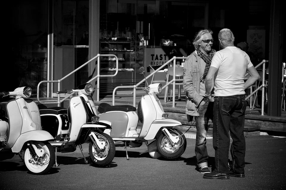 Two men talk beside a row of scooters — photograph by Peter Pickering