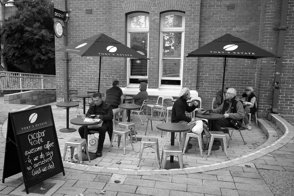 People sit at café tables beside a brick building — photograph by Peter Pickering