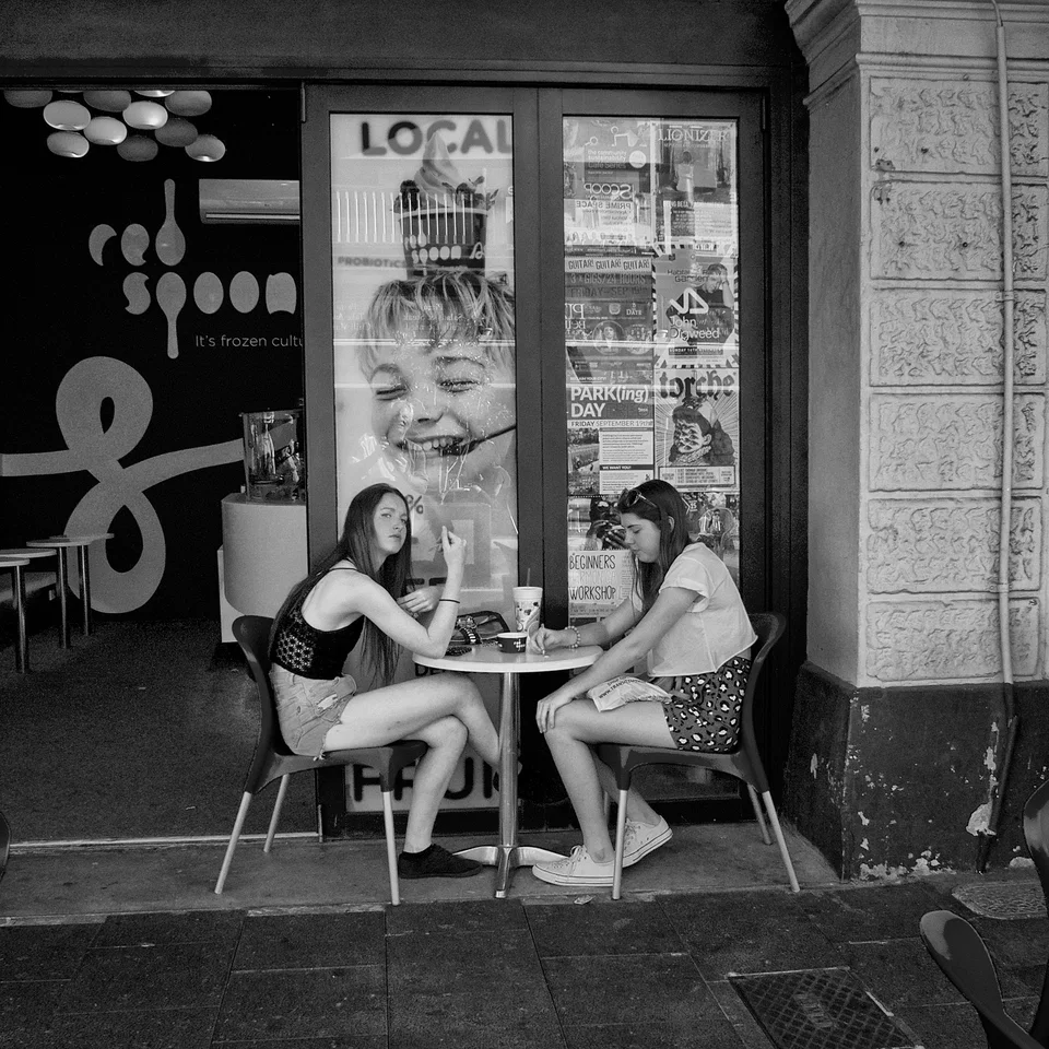 People sit outside a café beneath a large face in the window — photograph by Peter Pickering