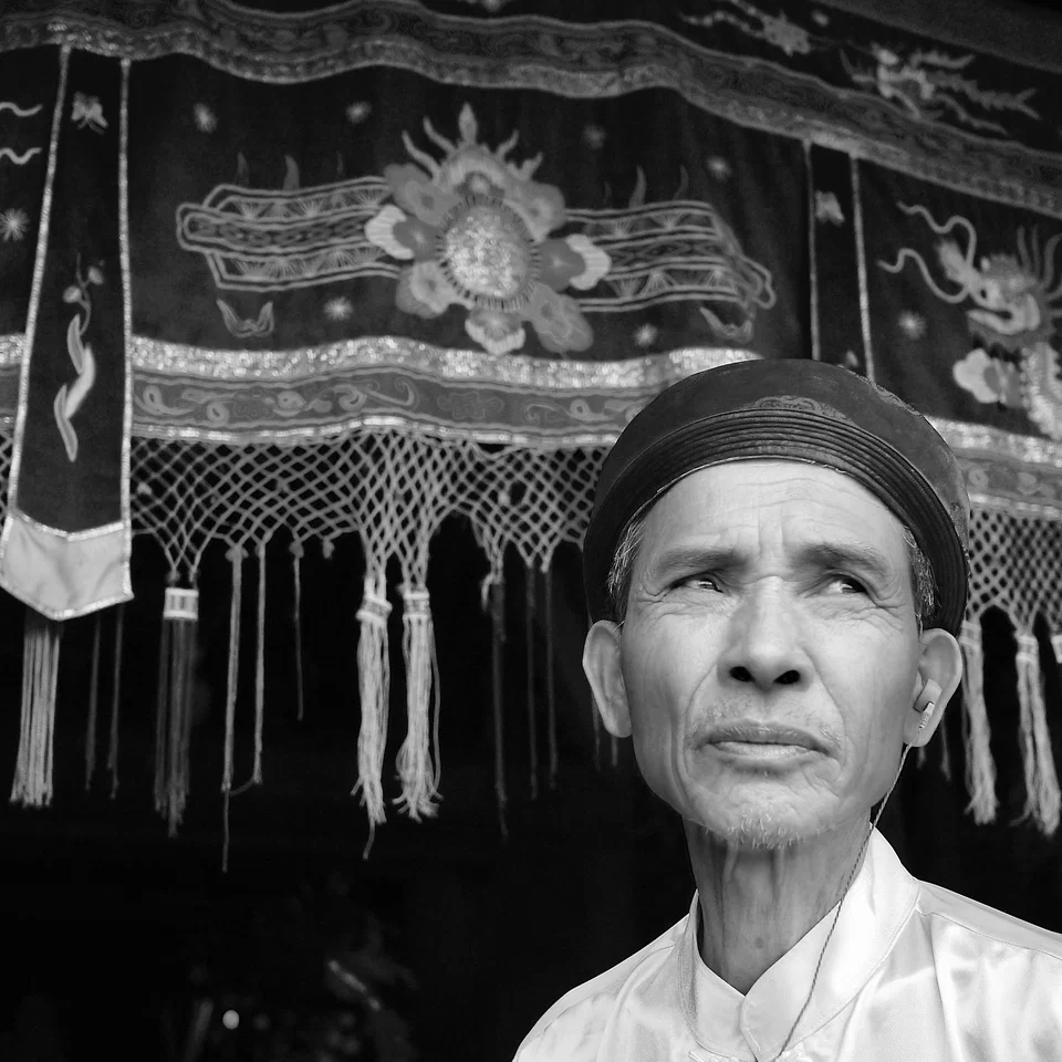 A man in traditional clothing before an ornate hanging — photograph by Peter Pickering