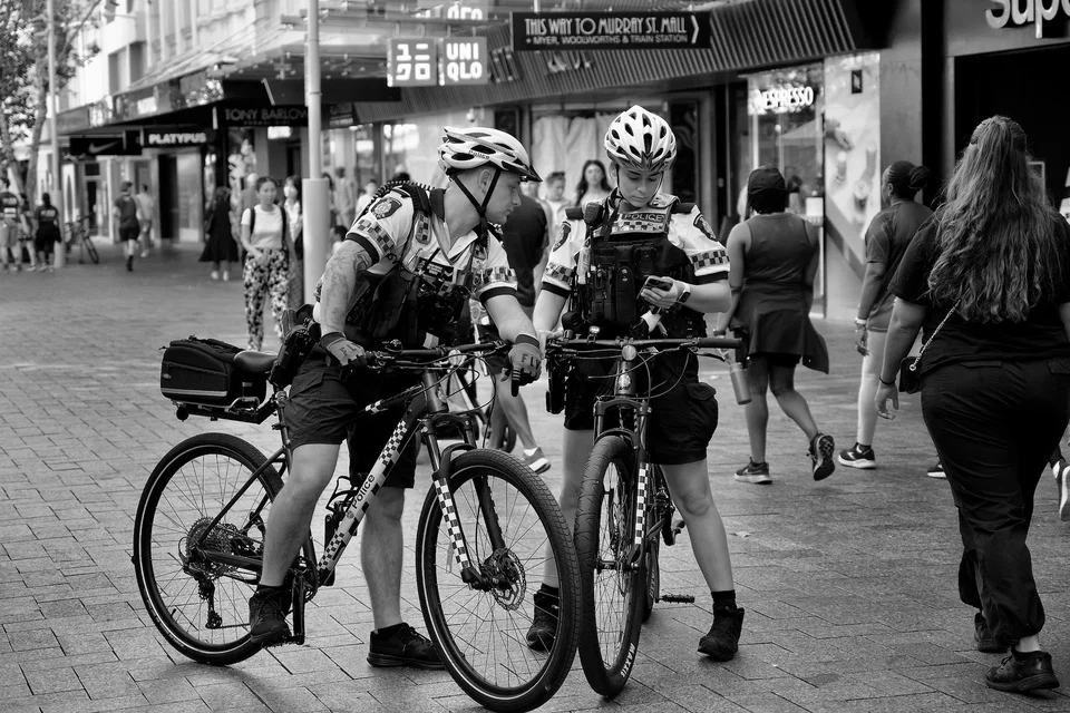 Two uniformed cyclists pause in a city shopping street — photograph by Peter Pickering