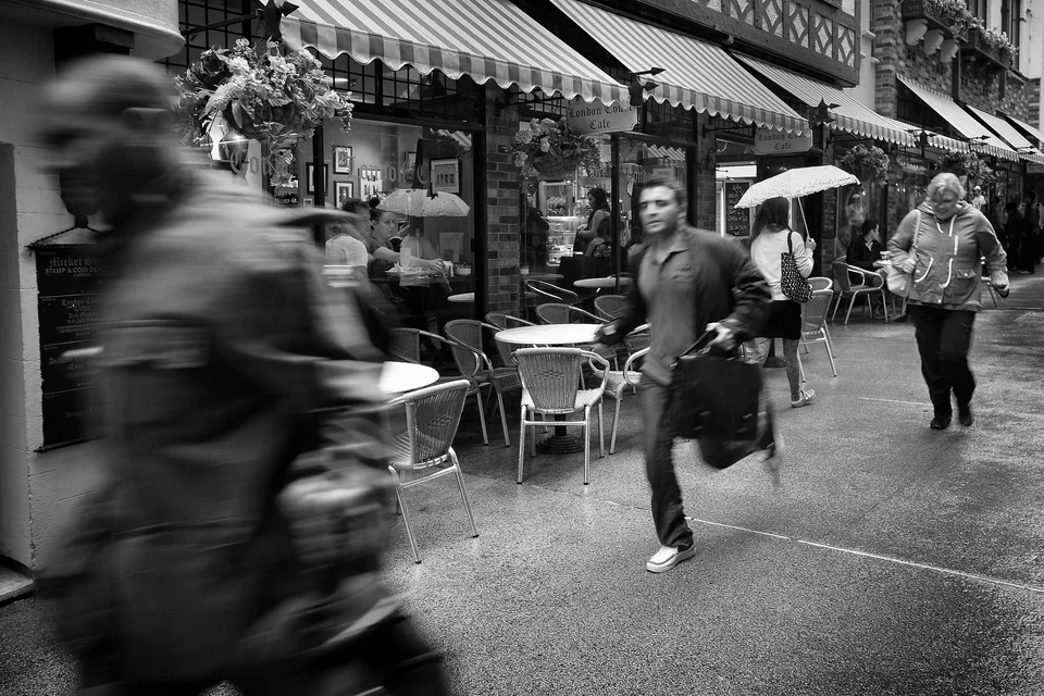 A runner and a blurred passer-by cross a shopping street — photograph by Peter Pickering
